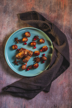 Vertical photo of few sweet rolls stuffed by cream with chocolate on ends. Sweets are on blue plate with several raw hazelnuts. Plate is on wooden board with vintage color.の写真素材
