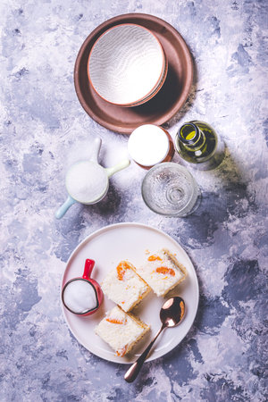 Vertical photo of few pieces of homemade cakes. Cake are from light dough with cream topping which is full of tangerine pieces. Cup with creamed milk is on the plate with spoon.の写真素材