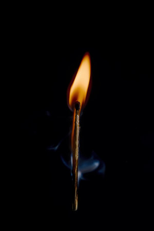 Vertical photo of match stick. The safety match has flaming hot head but the body is still fine. Nice curly smoke goes from head to the space. Background is black.の写真素材