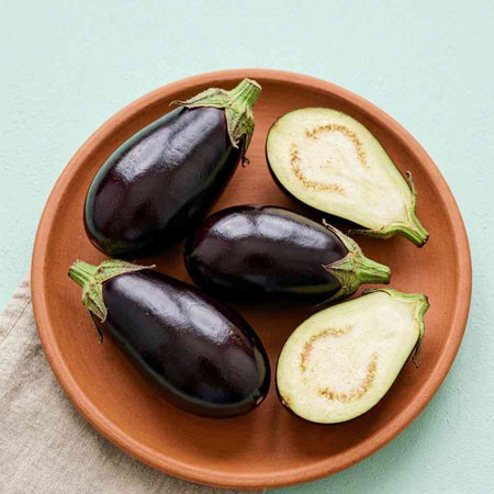 Fresh eggplants in a clay plate on a green background.