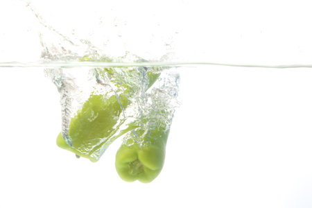 Close up green pepper fall into the water, white background.の写真素材