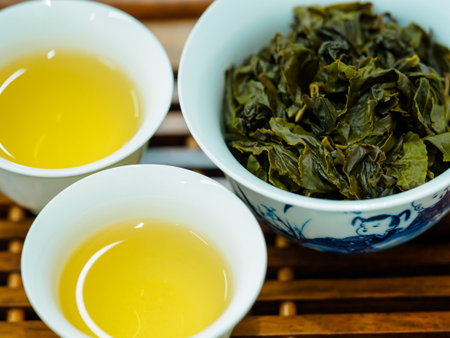 High angle close-up of two cups of green oolong tea and tea leaves on a wooden tray
