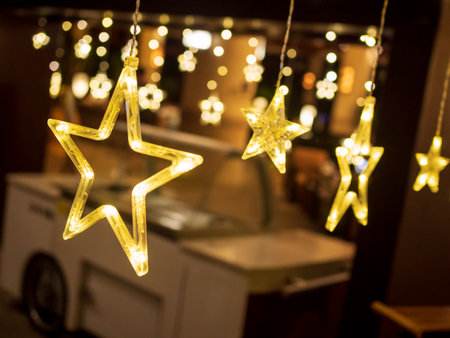 Diagonal row of electric lighted stars with warm yellow lights against a dark backdrop. Festive /...