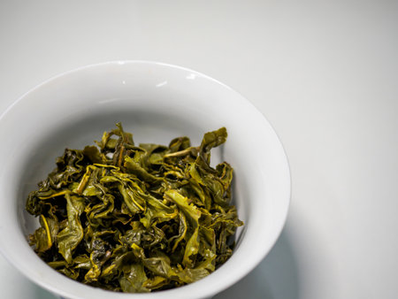 Close-up macro shot of wet / damp Chinese green oolong tea leaves in a porcelain cup / gaiwan with...