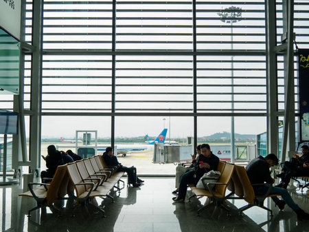 BAIYUN, GUANGZHOU, CHINA - 10 MAR 2019 - Passengers sit and wait at a boarding gate within Baiyun International Airport. A plane is visible in the background. Baiyun is one of the busiest airports in China.のeditorial素材