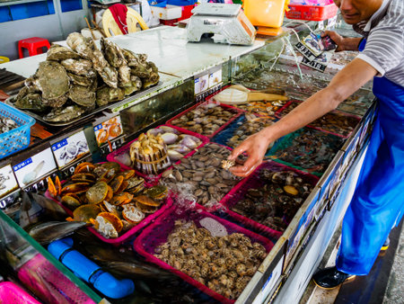 HAINAN, CHINA - 3 MAR 2019 â A vendor handles fresh live seafood (shellfish, oysters, mussels, clams) for sale at a seafood wholesale and retail centre in Hainan, Chinaのeditorial素材