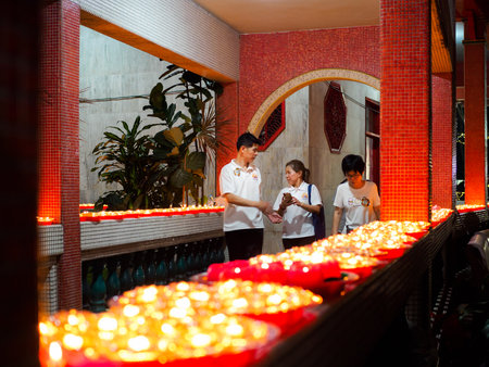 SINGAPORE, 18 MAY 2019 - A volunteer workers at Bright Hill buddhist temple walk past a row of Buddhist oil lamps on Vesak Day. Oil lamps symbolise wisdom and enlightenment in Buddhismのeditorial素材