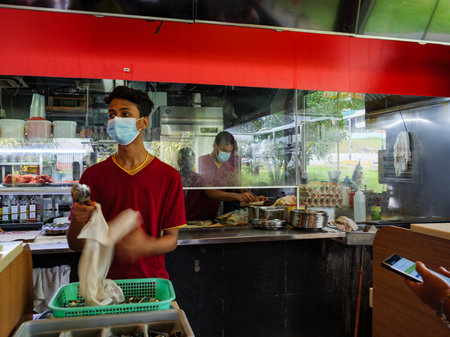 SINGAPORE â JULY 10 2020 â Employees at the Springleaf Prata Place Indian restaurant in Singapore wear protective masks as they clean cutlery and prepare food as prevention against covid-19 transmissionのeditorial素材