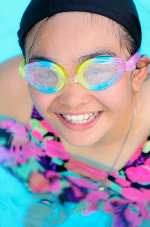 Young girl smiling and having fun swimming in a pool with blue waterの写真素材