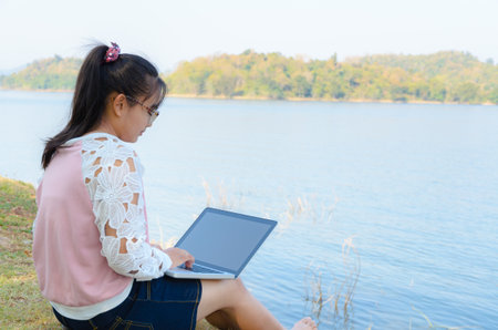 Young girl with laptop sitting on the riverbank in parkの写真素材