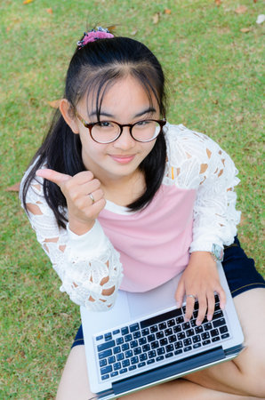 Lovely girl is happy with a laptop on lawn in parkの写真素材