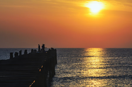 Silhouette fisherman on the old wooden bridge and sea at sunrise in rural Thailand.の写真素材