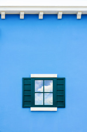 Sky and cloud reflection in green window glass on blue wall of house, Italy retro styleの写真素材
