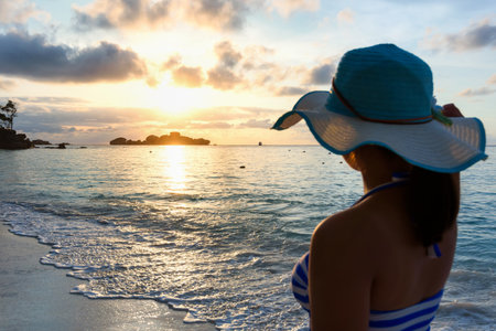 Girl with blue and white striped swimsuit standing watch nature sky and sea during the sunrise on beach of Honeymoon Bay at Koh Miang, Similan Islands National Park, Phang Nga, Thailandの写真素材