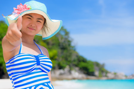 Tourist girl in blue white swimsuit standing thumb up praising the natural beauty of the sea on beach during summer at Koh Miang Island, Mu Ko Similan National Park, Phang Nga Province, Thailandの写真素材