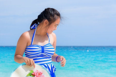 Tourist girl in a blue white striped swimsuit standing with happiness on the beautiful beach and sea during summer at Koh Miang Island, Mu Ko Similan National Park, Phang Nga province, Thailandの写真素材