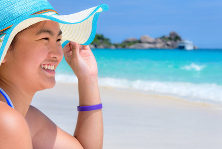 Girl in a blue swimwear sitting a happy on the beach with the sea as background during summer at Koh Miang Island, Mu Ko Similan National Park, Phang Nga province, Thailandの写真素材