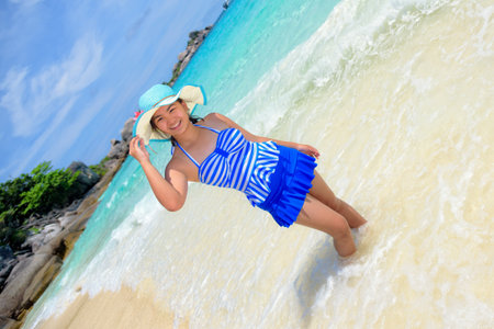 Photos tilt of beautiful woman in a blue striped swimsuit and hat standing on beach of sea at Koh Miang Island during summer in Mu Ko Similan National Park, Phang Nga, Thailandの写真素材