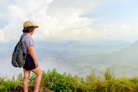 Traveler teens girl hiker wear caps and glasses with backpack looking beautiful nature landscape on high mountain at viewpoint of Phu Chi Fa Forest Park during sunset in Chiang Rai Province Thailandの写真素材