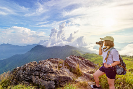 Hiker asian teen girl wear cap and eyeglass with happy holding dslr camera shooting photo beautiful nature in winter on peak mountain at sunset in Phu Chi Fa Forest Park, Chiang Rai, Thailandの写真素材