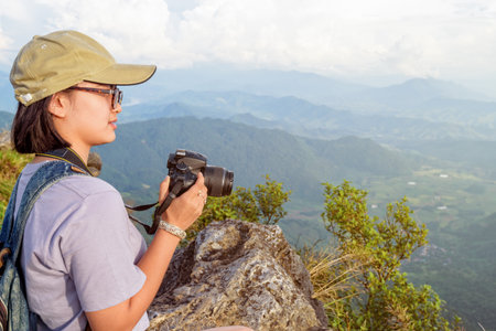 Hiker asian teen girl wear cap and eyeglass with happy holding dslr camera for photography beautiful natural in winter on peak mountain at Phu Chi Fa Forest Park, Chiang Rai, Thailandの写真素材