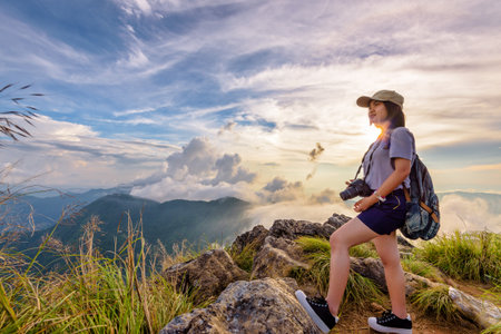 Hiker asian young woman happy with camera backpack and caps looking beautiful landscape nature of mountain and colourful sky at sunset on viewpoint Phu Chi Fa Forest Park, Chiang Rai, Thailandの写真素材