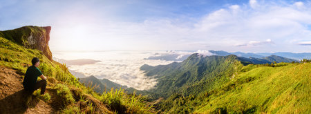Panorama beautiful landscape nature, Male tourist are watching the sunrise on peak mountain with sun cloud fog and bright sky in winter at Phu Chi Fa Forest Park, famous attraction of Chiang Rai Province, Thailandの写真素材