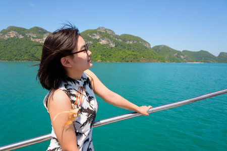 Cute young woman with eyeglasses smiling happily on the boat while cruising the beautiful natural of the blue sea and sky in summer at Mu Ko Ang Thong National Park, Surat Thani, Thailandの写真素材