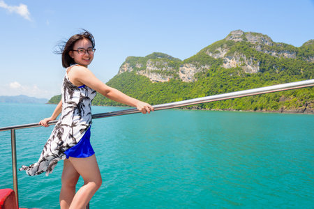Asian young woman with eyeglasses smiling happily on the boat while cruising the beautiful natural of the blue sea and sky in summer at Mu Ko Ang Thong National Park, Surat Thani, Thailandの写真素材