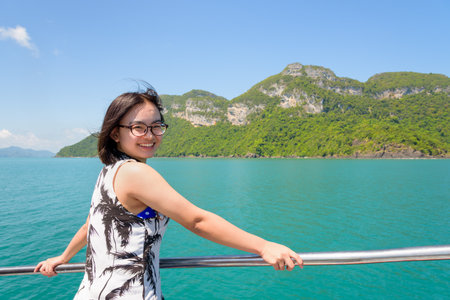 Asian young woman with eyeglasses smiling happily on the boat while cruising the beautiful natural of the blue sea and sky in summer at Mu Ko Ang Thong National Park, Surat Thani, Thailandの写真素材