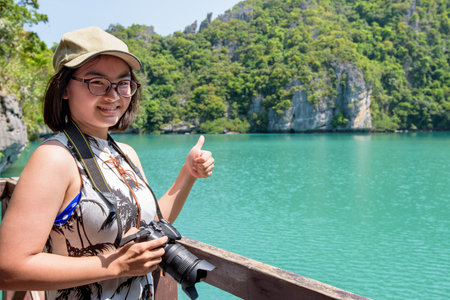Woman tourist at Thale Nai holding camera and thumbs up after taking pictures of Lagoon (Emerald Lake) on Koh Mae Ko island in Mu Ko Ang Thong National Park, Surat Thani, Thailandの写真素材
