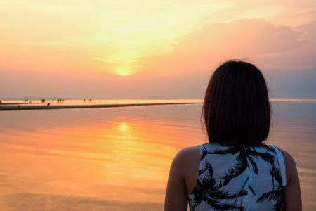 Young woman are standing watching the beautiful natural landscape, colorful of the sky and the sea during a sunset on the beach at Nathon Sunset Viewpoint in Ko Samui island, Surat Thani, Thailandの写真素材