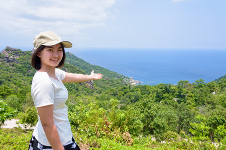 Women tourists raise hand invite to see the beautiful nature landscape blue sea under the summer sky from high scenic viewpoint at Koh Tao attraction in the Gulf of Thailand, Surat Thani, Thailandの写真素材
