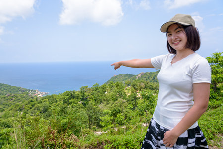 Women tourists raise hand and pointing the finger at the sea on high viewpoint to see the beautiful nature landscape of Koh Tao island is a famous attractions in Surat Thani, Thailandの写真素材