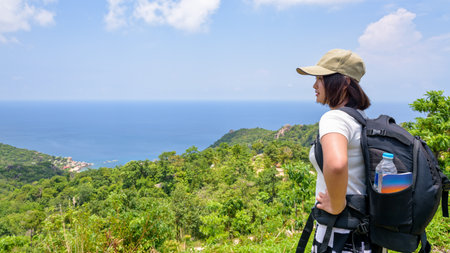 Women tourist with a backpack wear cap standing look at beautiful nature landscape blue sea and sky from high scenic viewpoint at Koh Tao in Surat Thani, Thailand, 16:9 widescreenの写真素材