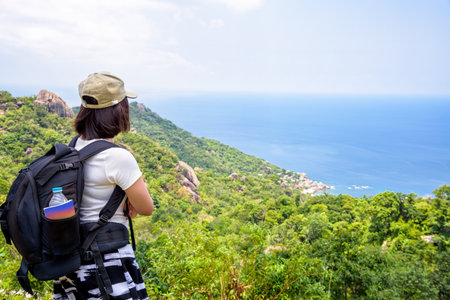 Women tourist with a backpack wear cap standing look at beautiful nature landscape blue sea under the summer sky from high scenic viewpoint at Koh Tao in Surat Thani, Thailandの写真素材