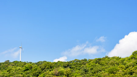 Wind Turbine Generator clean electrical energy set on the mountain amidst nature of green tree and blue sky for background, 16:9 widescreenの写真素材