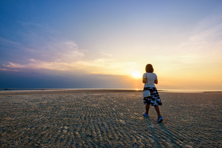 Young woman tourist strolling on the beach watching the beautiful natural landscape, colorful of the sky and the sea during a sunset at Nathon Sunset Viewpoint in Ko Samui, Surat Thani, Thailandの写真素材