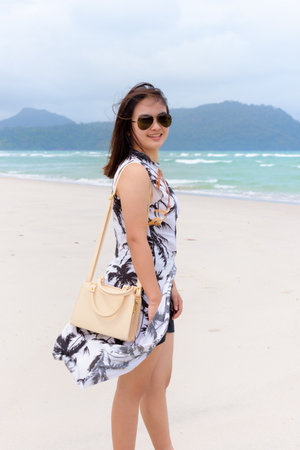Beautiful woman tourist wearing sunglasse smiling looking at the camera on the beach and the sea in summer at Koh Tarutao island National Park, Satun, Thailandの写真素材