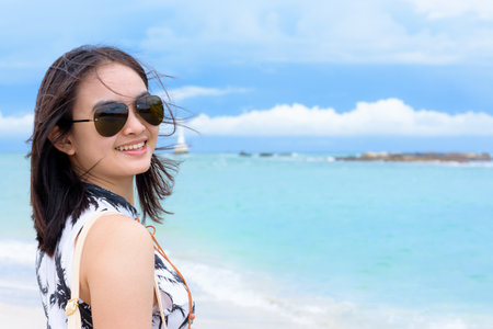 Beautiful woman tourist wearing sunglasse looking at the camera and smiling with happy on the beach and sea in summer sky background at Koh Tarutao island, Satun, Thailandの写真素材