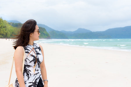 Beautiful woman tourist wearing sunglasse smiling looking at the nature landscape of the beach and the sea in summer sky on Tarutao island National Park, Satun, Thailandの写真素材