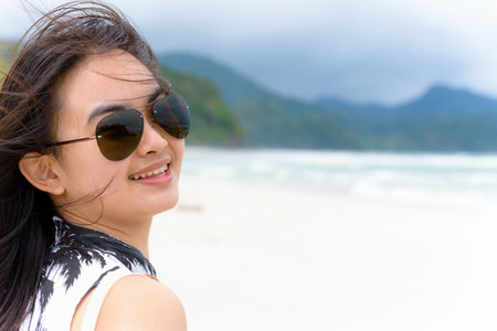 Close-up face beautiful woman tourist wearing sunglasse looking at the camera and smiling with happy on the beach and sea in summer at Tarutao island, Satun, Thailandの写真素材