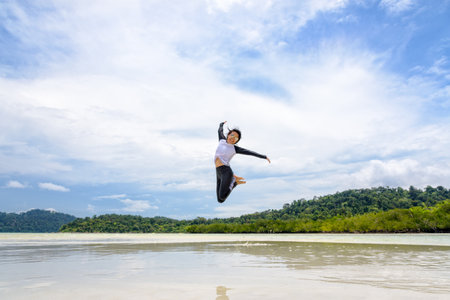 Happy asian young woman wearing sunglasses jumping fun on the beach of Ko Ra Wi on the blue sky by...