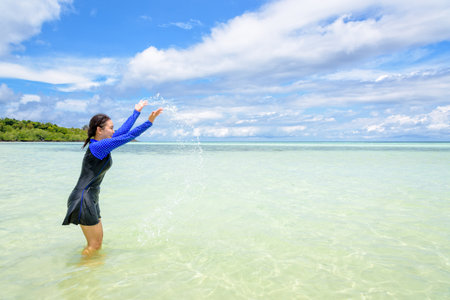 Happy asian teen girl in a swimsuit play splashing water in the sea with fun under the blue sky of Ko Ra Wi on tour vacation summer holiday at Ko Lipe island, Tarutao National Park, Satun, Thailandの写真素材