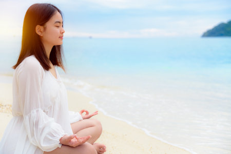 Beautiful asian young woman practice yoga on the beach near the sea under sunlight at sunrise, Relaxation for health in the midst of nature with happiness and peace, blank for the backgroundの写真素材