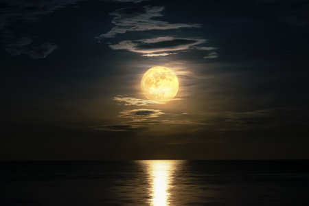 Super full moon and cloud in the yellow sky above the ocean horizon at midnight, moonlight reflect...