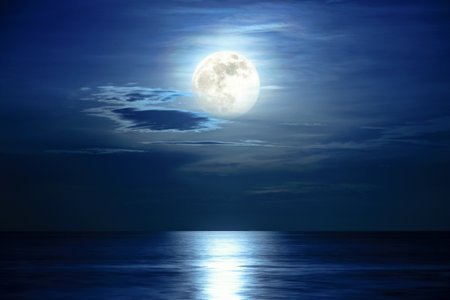 Super full moon and cloud in the blue sky above the ocean horizon at midnight, moonlight reflect the water surface and wave, Beautiful nature landscape view at night scene of the sea for backgroundの写真素材