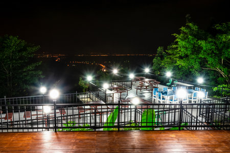 Night scene high angle viewpoint beautiful nature landscape and road lights at night. Table chairs and light lamp on the terrace for dinner of the restaurant on the mountain, Chon Buri, Thailandの写真素材