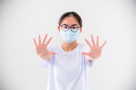 Portrait Asian young woman wears glasses and mask to protect against Coronavirus looking at camera, girl show hands stop coronavirus outbreak isolated on white background stop virus Covid 19 conceptの写真素材