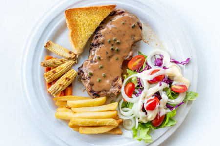 Closeup top view steak pork chop with creamy pepper sauce, Served with french fries, toast, grill baby corn, roast carrot, and vegetables salad on a clean white dish for cooking delicious mealsの写真素材